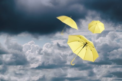 Image of Yellow umbrellas flying in cloudy sky. Stormy weather