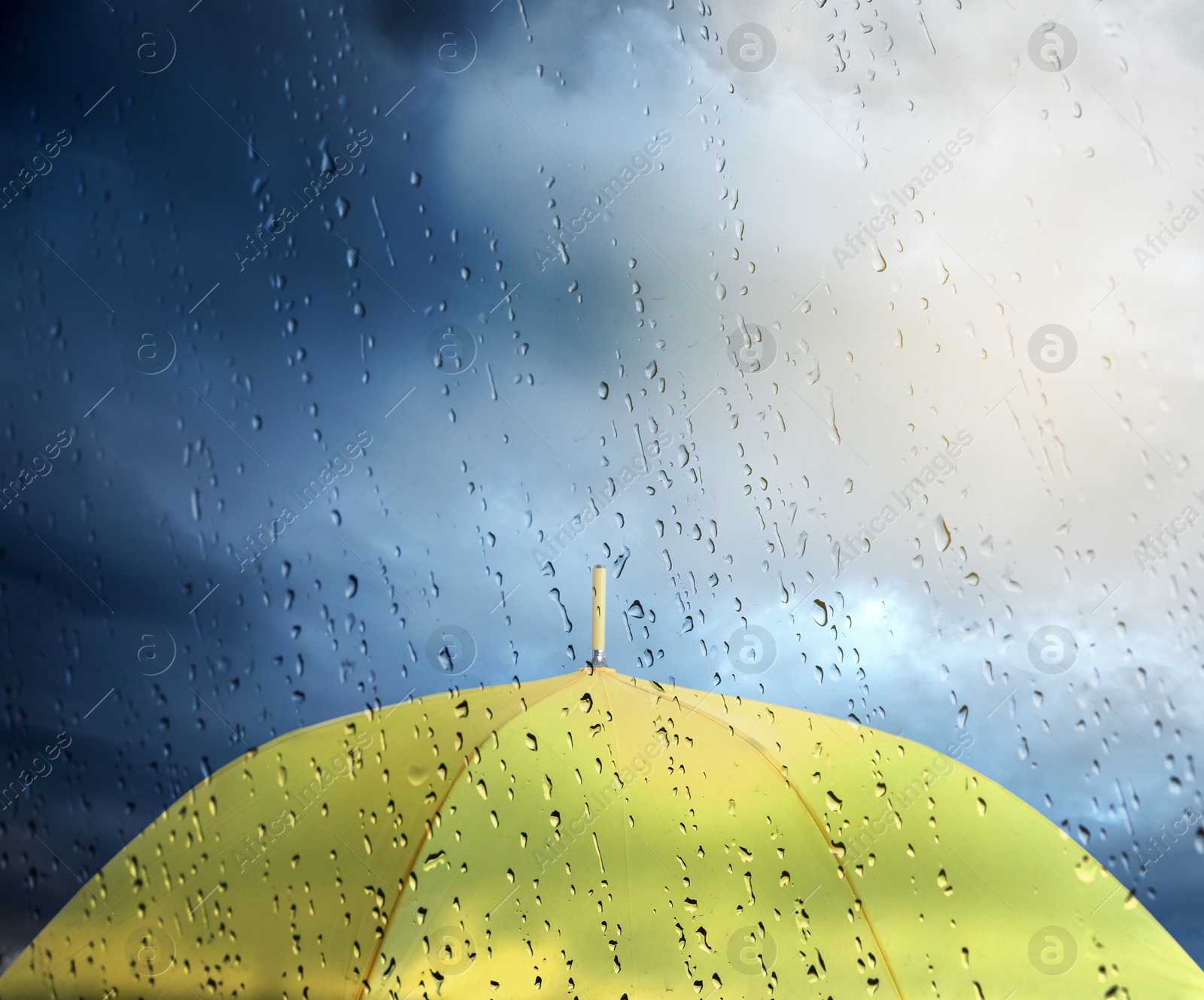 Yellow umbrella under cloudy sky, view through wet window. Stormy weather Image of Yellow umbrella under cloudy sky, view through wet window. Stormy weather