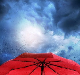 Image of Red umbrella under cloudy sky, view through wet window. Stormy weather