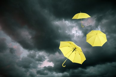 Image of Yellow umbrellas flying in dark cloudy sky. Stormy weather