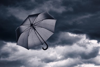 Image of Black umbrella flying in dark cloudy sky. Stormy weather
