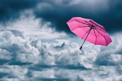 Image of PInk umbrella flying in cloudy sky. Stormy weather