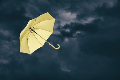 Image of Yellow umbrella flying in dark cloudy sky. Stormy weather