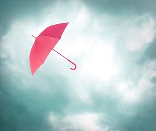 Image of Pink umbrella flying in cloudy sky. Stormy weather