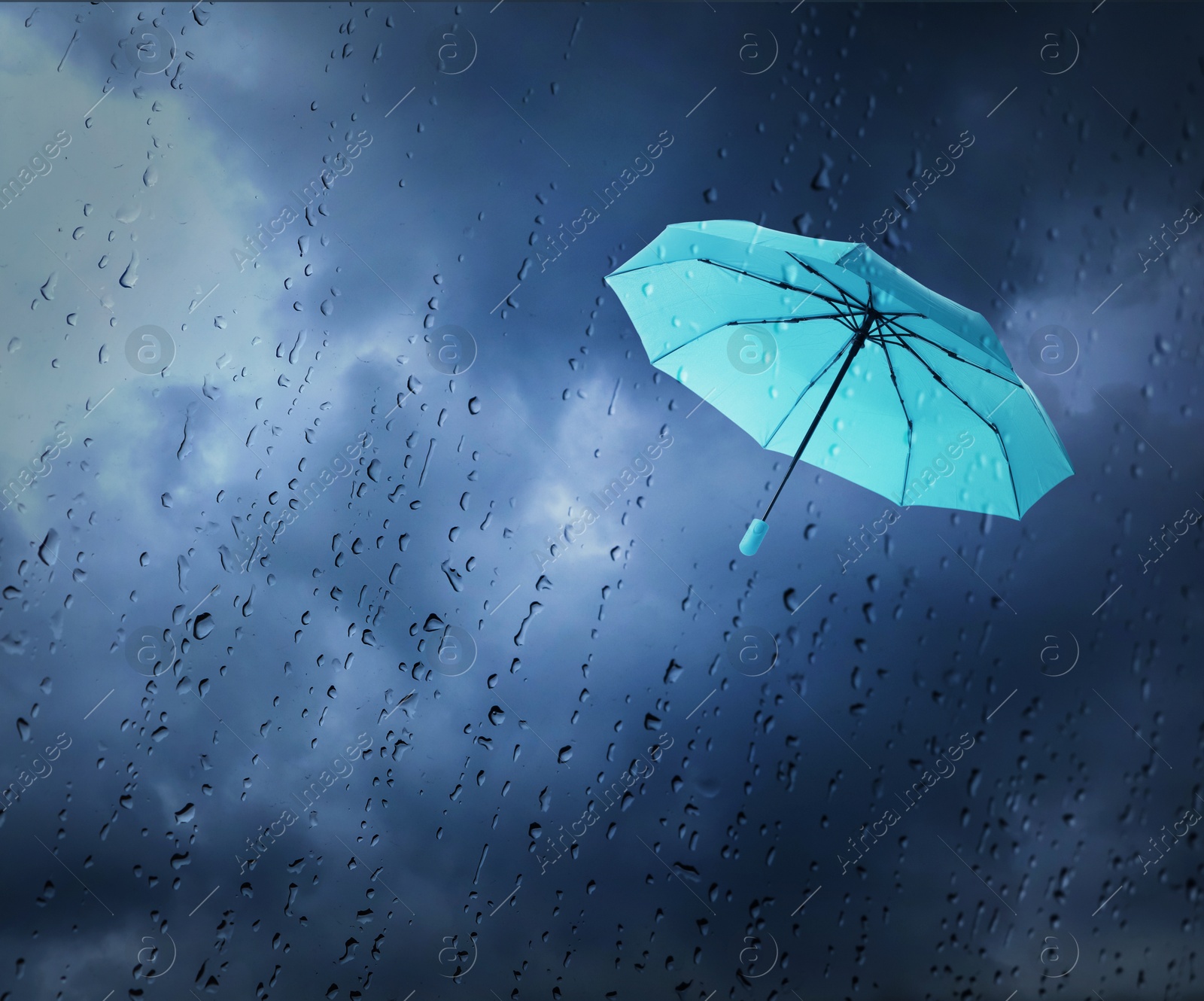 Light blue umbrella flying in dark cloudy sky, view through wet window. Stormy weather Image of Light blue umbrella flying in dark cloudy sky, view through wet window. Stormy weather