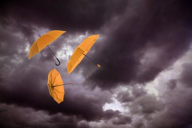 Image of Orange umbrellas flying in dark cloudy sky. Stormy weather