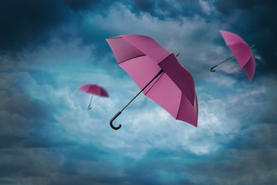 Image of Pink umbrellas flying in cloudy sky. Stormy weather
