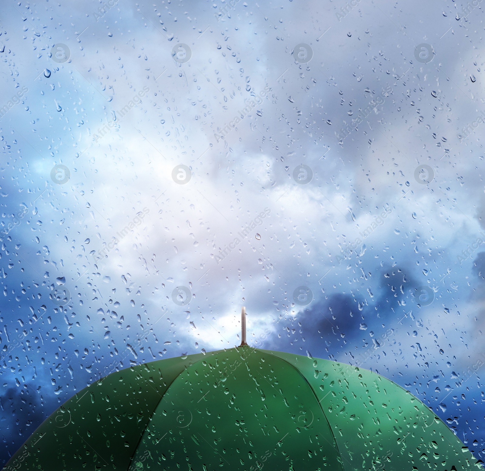 Green umbrella under cloudy sky, view through wet window. Stormy weather Image of Green umbrella under cloudy sky, view through wet window. Stormy weather