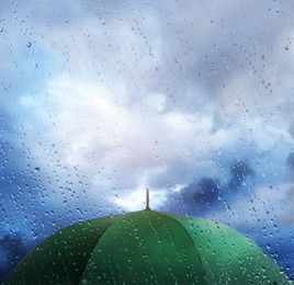 Image of Green umbrella under cloudy sky, view through wet window. Stormy weather