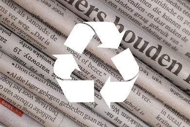 Image of Recycling symbol and many newspapers in different languages as background, closeup. Eco-friendly lifestyle, reusing