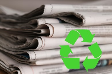 Image of Recycling symbol and many newspapers on table, closeup. Eco-friendly lifestyle, reusing