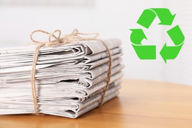 Image of Recycling symbol and stack of tied newspapers on wooden table, closeup. Eco-friendly lifestyle, reusing