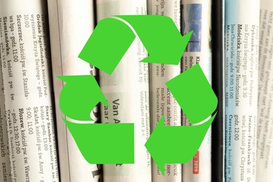 Image of Recycling symbol and many newspapers in different languages as background, closeup. Eco-friendly lifestyle, reusing