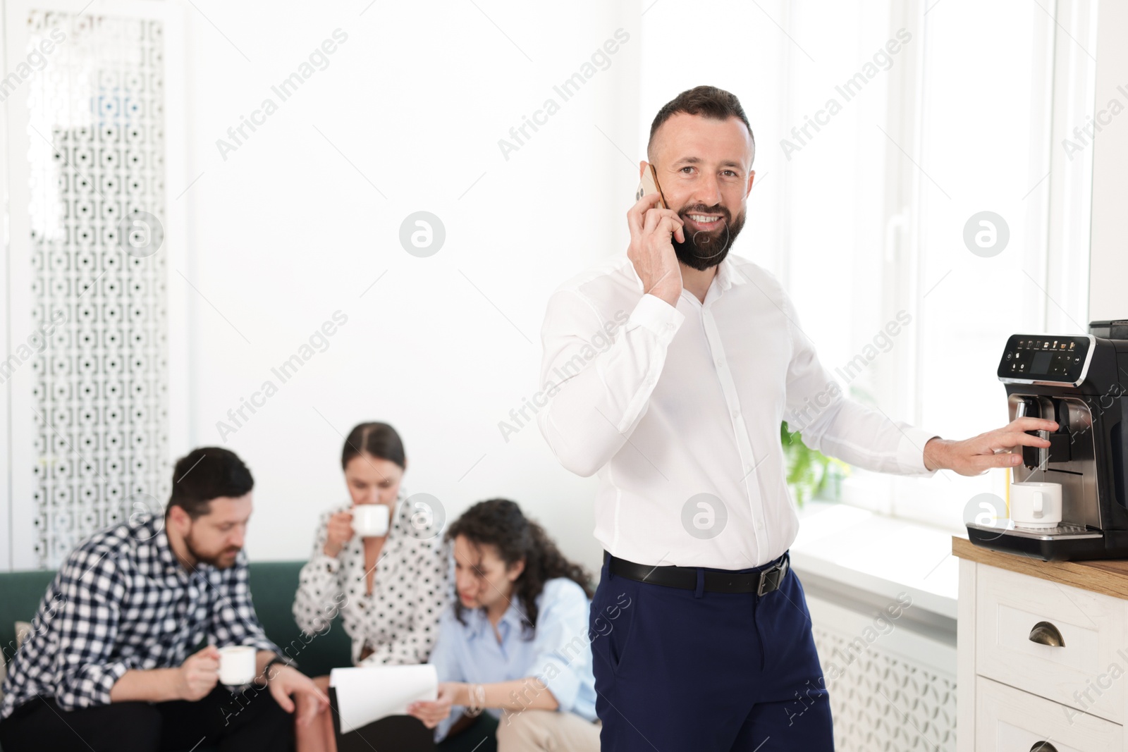 Man talking on phone while making coffee. Colleagues having break in office Photo of Man talking on phone while making coffee. Colleagues having break in office