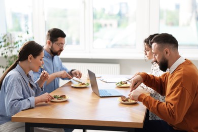 Photo of Colleagues eating and chatting during lunch break in office