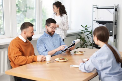 Photo of Colleagues eating and discussing work during lunch break in office