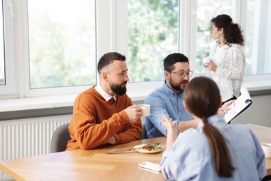 Photo of Colleagues eating and discussing work during lunch break in office