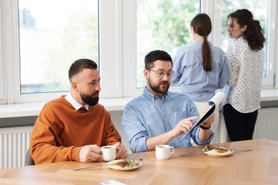 Photo of Colleagues eating and discussing work during lunch break in office