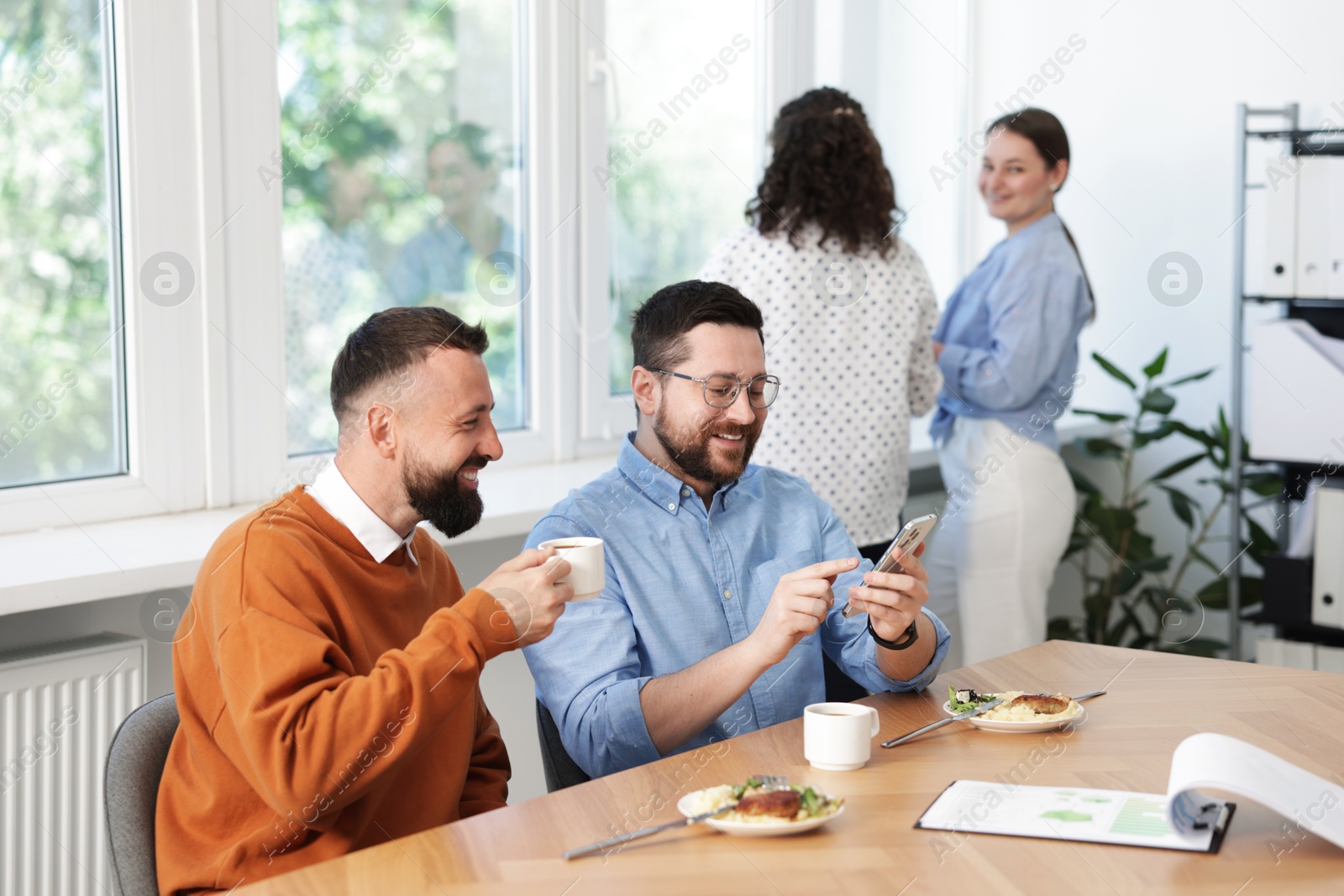 Man showing his colleague something on smartphone during lunch break in office Photo of Man showing his colleague something on smartphone during lunch break in office