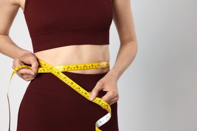 Photo of Woman measuring her belly with tape on gray background, closeup. Space for text