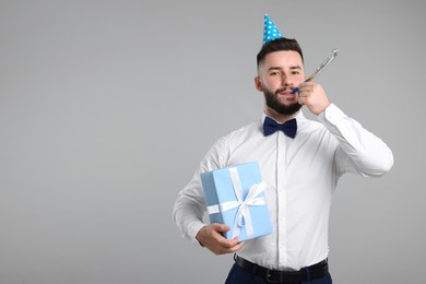 Photo of Happy Birthday. Handsome man with party hat, blower and gift box on grey background, space for text