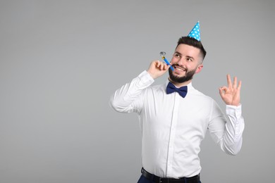 Photo of Happy Birthday. Handsome man with party hat and blower showing ok gesture on grey background, space for text