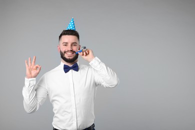 Photo of Happy Birthday. Handsome man with party hat and blower showing ok gesture on grey background, space for text