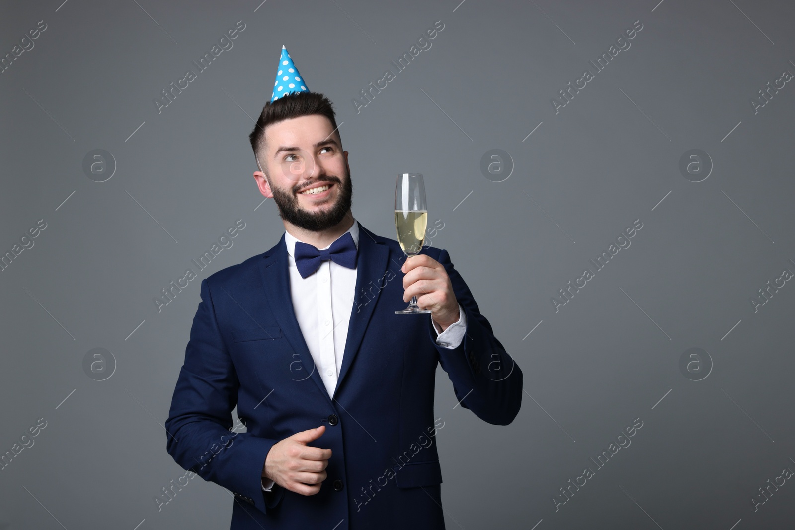 Happy Birthday. Handsome man with party hat and glass of champagne on grey background, space for text Photo of Happy Birthday. Handsome man with party hat and glass of champagne on grey background, space for text