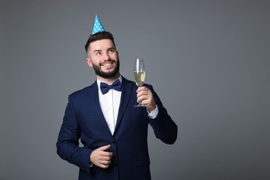 Photo of Happy Birthday. Handsome man with party hat and glass of champagne on grey background, space for text