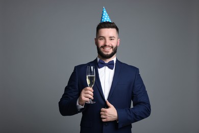 Photo of Happy Birthday. Handsome man with party hat and glass of champagne on grey background