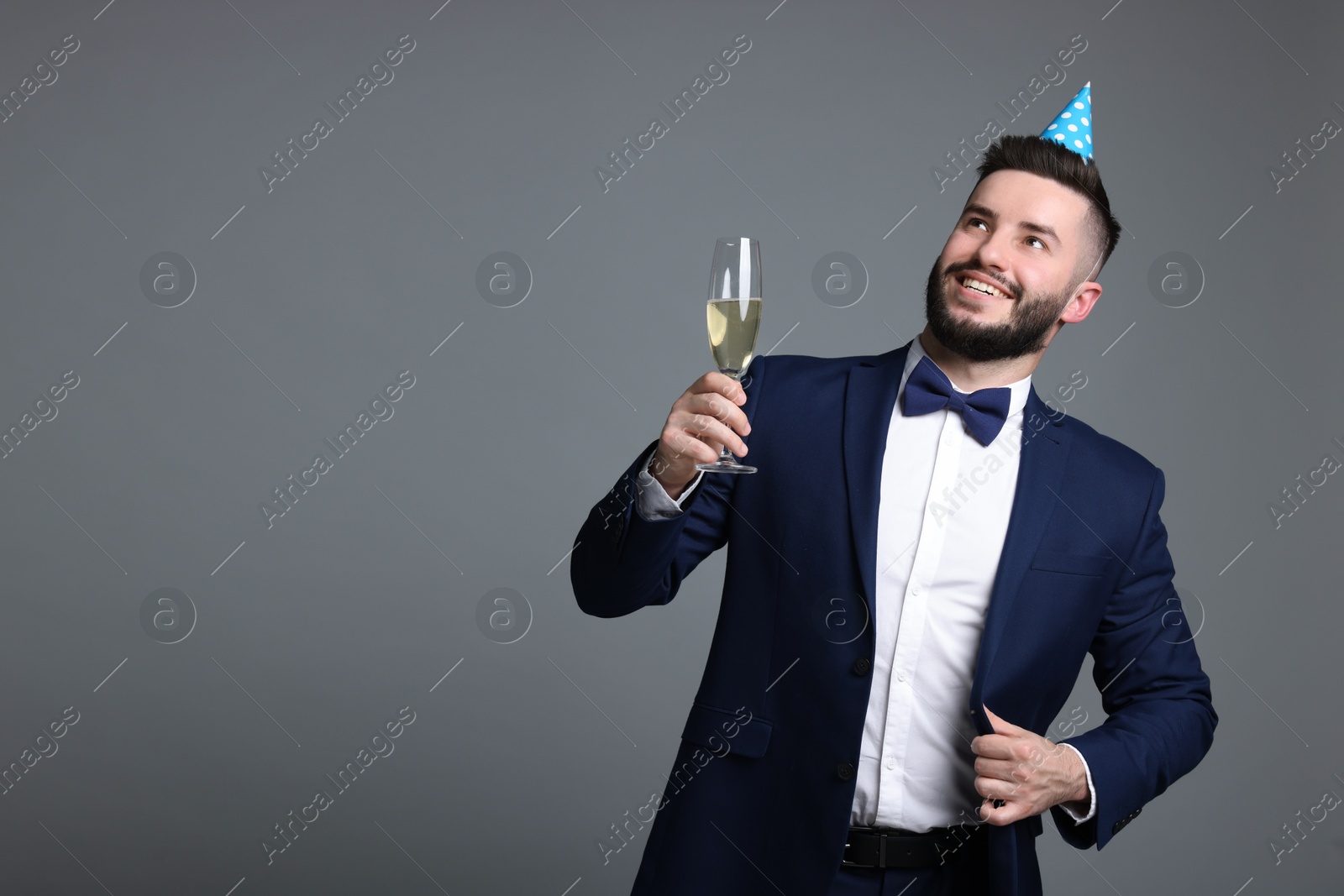 Happy Birthday. Handsome man with party hat and glass of champagne on grey background, space for text Photo of Happy Birthday. Handsome man with party hat and glass of champagne on grey background, space for text