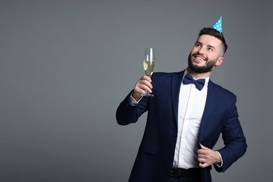Photo of Happy Birthday. Handsome man with party hat and glass of champagne on grey background, space for text