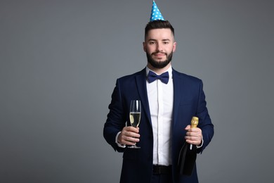 Photo of Happy Birthday. Handsome man with party hat and champagne on grey background, space for text