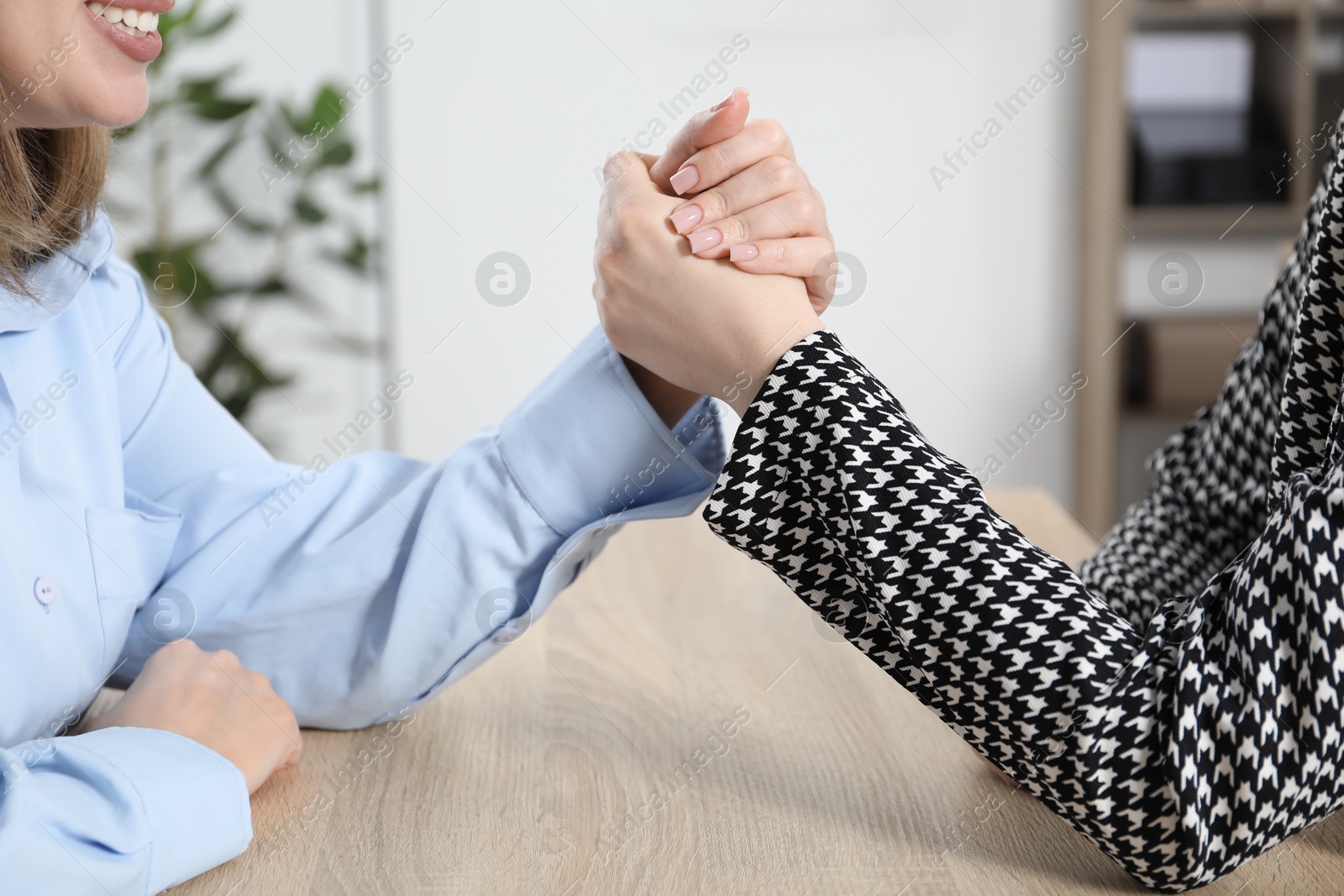 Businesswomen arm wrestling at wooden table in office, closeup Photo of Businesswomen arm wrestling at wooden table in office, closeup