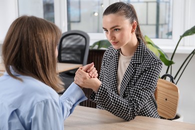 Photo of Businesswomen arm wrestling at wooden table in office