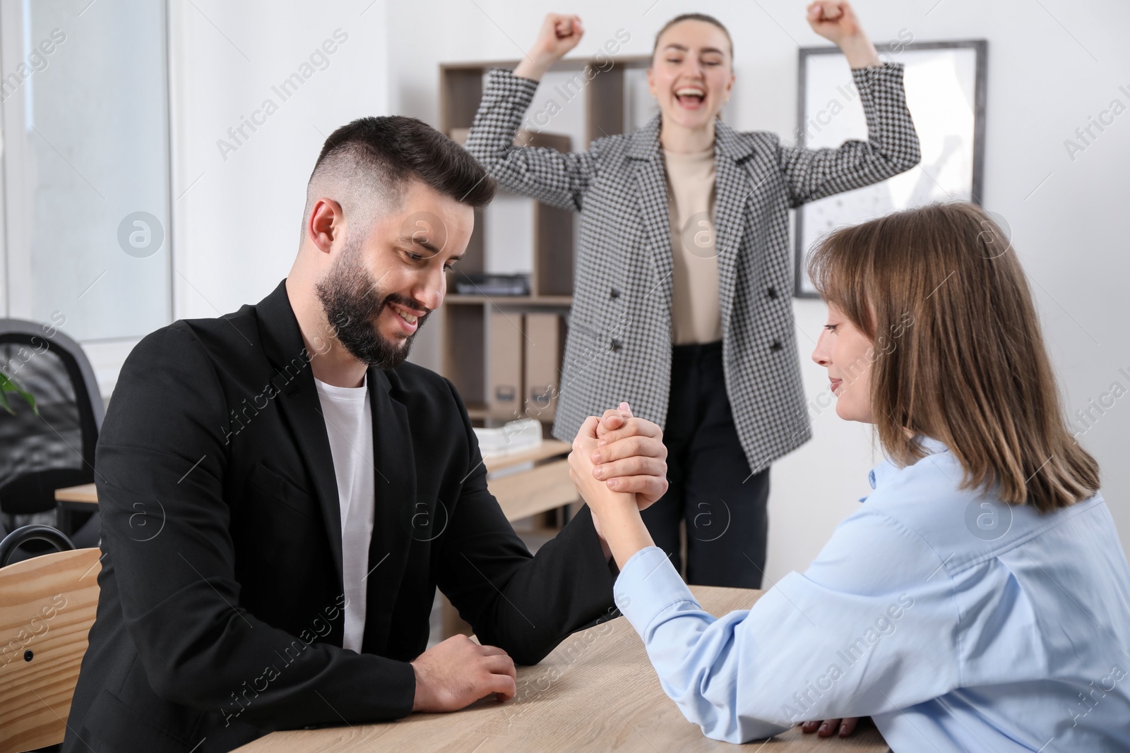 Businesspeople arm wrestling at wooden table in office, selective focus Photo of Businesspeople arm wrestling at wooden table in office, selective focus