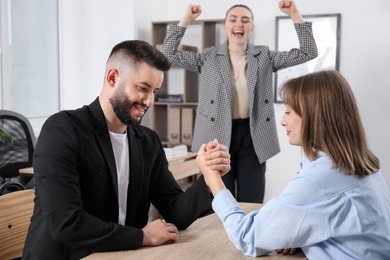 Photo of Businesspeople arm wrestling at wooden table in office, selective focus