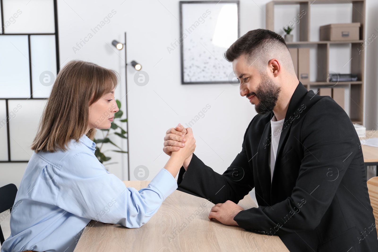 Businesspeople arm wrestling at wooden table in office Photo of Businesspeople arm wrestling at wooden table in office