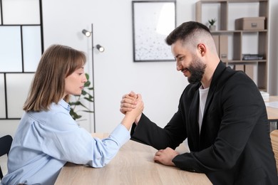 Photo of Businesspeople arm wrestling at wooden table in office