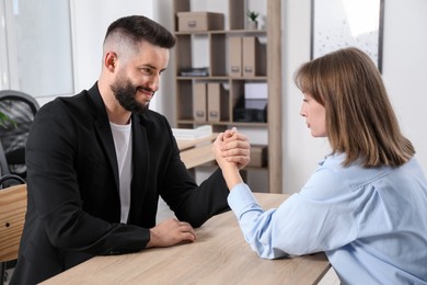 Photo of Businesspeople arm wrestling at wooden table in office