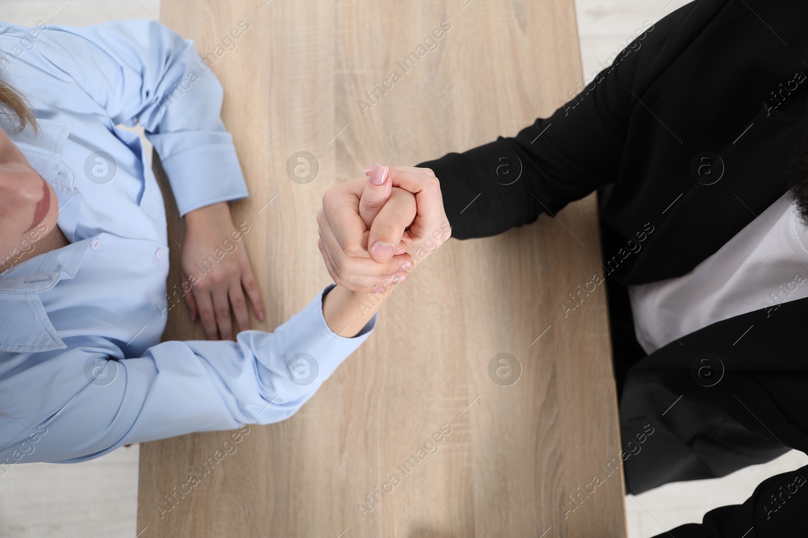 Businesspeople arm wrestling at wooden table in office, top view Photo of Businesspeople arm wrestling at wooden table in office, top view
