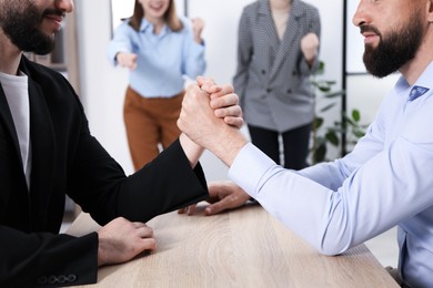 Photo of Businessmen arm wrestling at wooden table in office, closeup