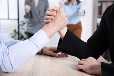 Photo of Businessmen arm wrestling at wooden table in office, closeup