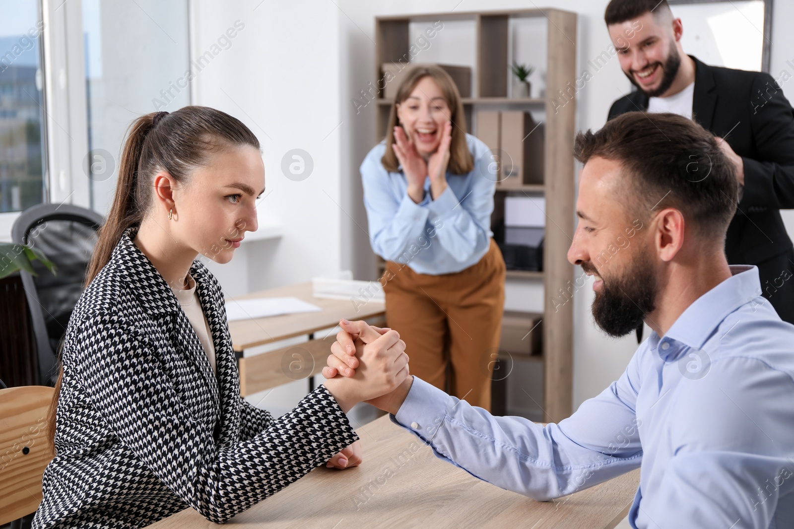 Businesspeople arm wrestling at wooden table in office, selective focus Photo of Businesspeople arm wrestling at wooden table in office, selective focus