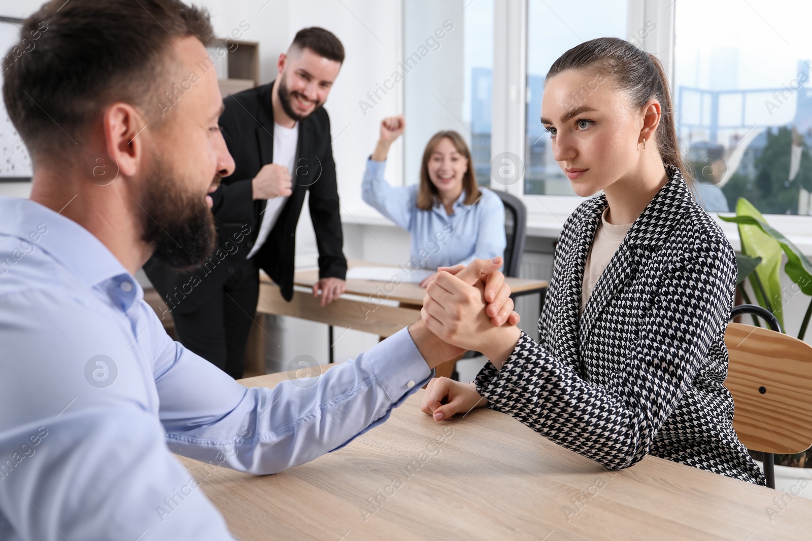 Businesspeople arm wrestling at wooden table in office, selective focus Photo of Businesspeople arm wrestling at wooden table in office, selective focus