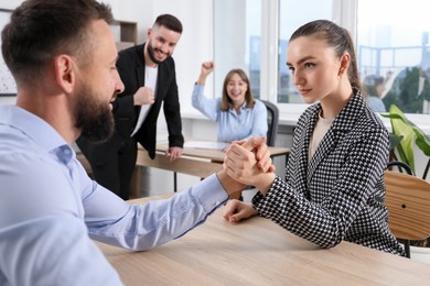 Photo of Businesspeople arm wrestling at wooden table in office, selective focus