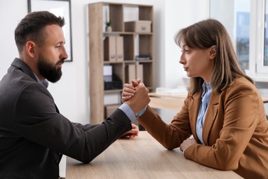 Photo of Businesspeople arm wrestling at wooden table in office