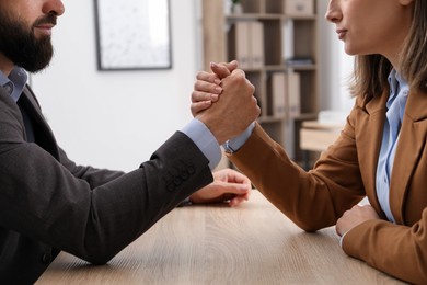 Photo of Businesspeople arm wrestling at wooden table in office, closeup