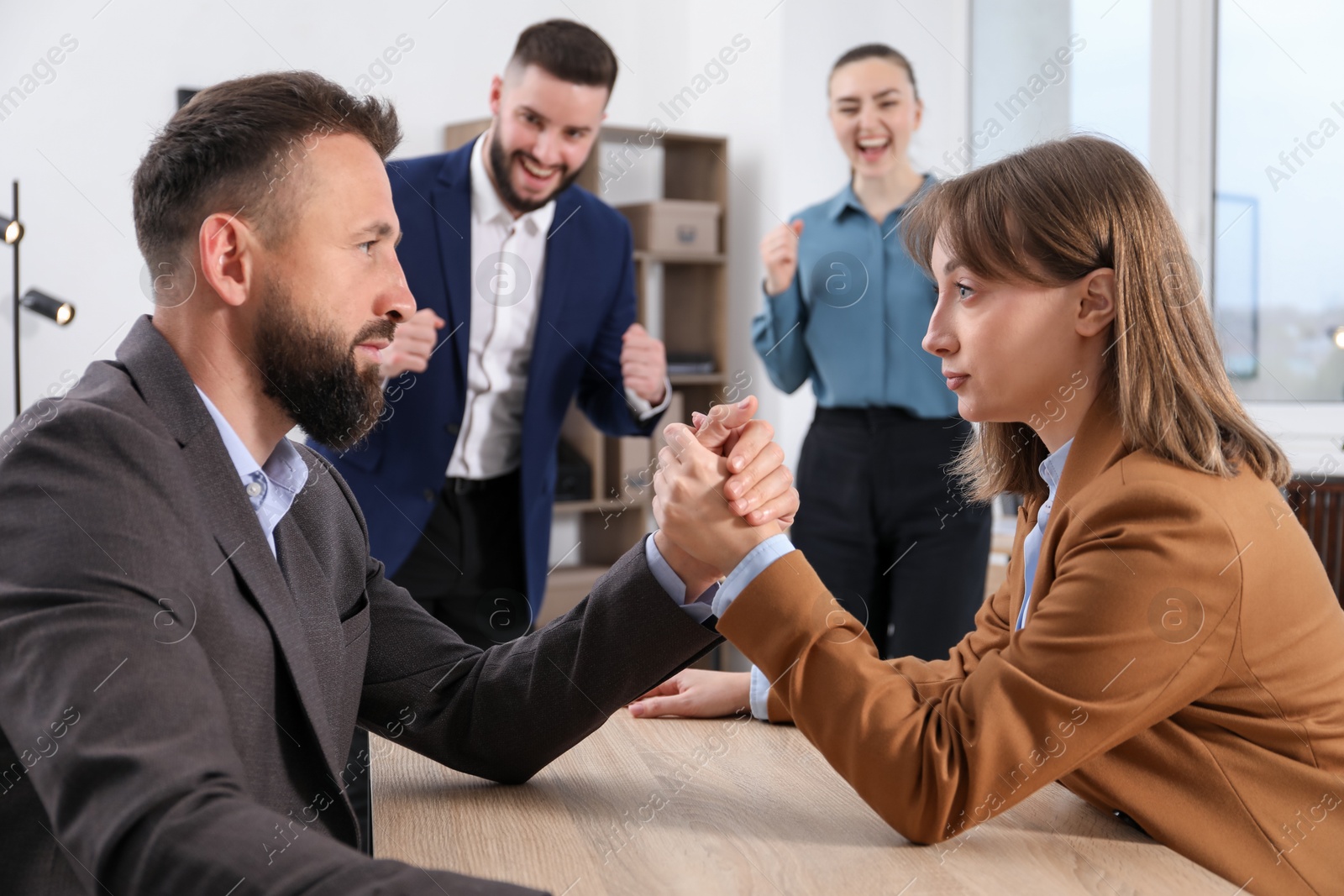 Businesspeople arm wrestling at wooden table in office, selective focus Photo of Businesspeople arm wrestling at wooden table in office, selective focus