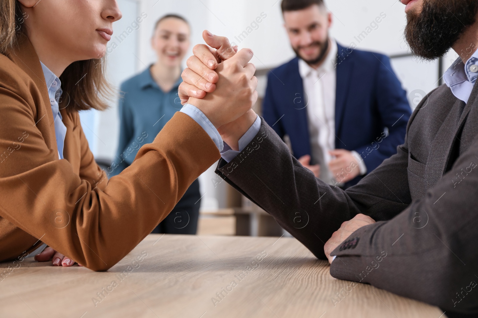 Businesspeople arm wrestling at wooden table in office, selective focus Photo of Businesspeople arm wrestling at wooden table in office, selective focus